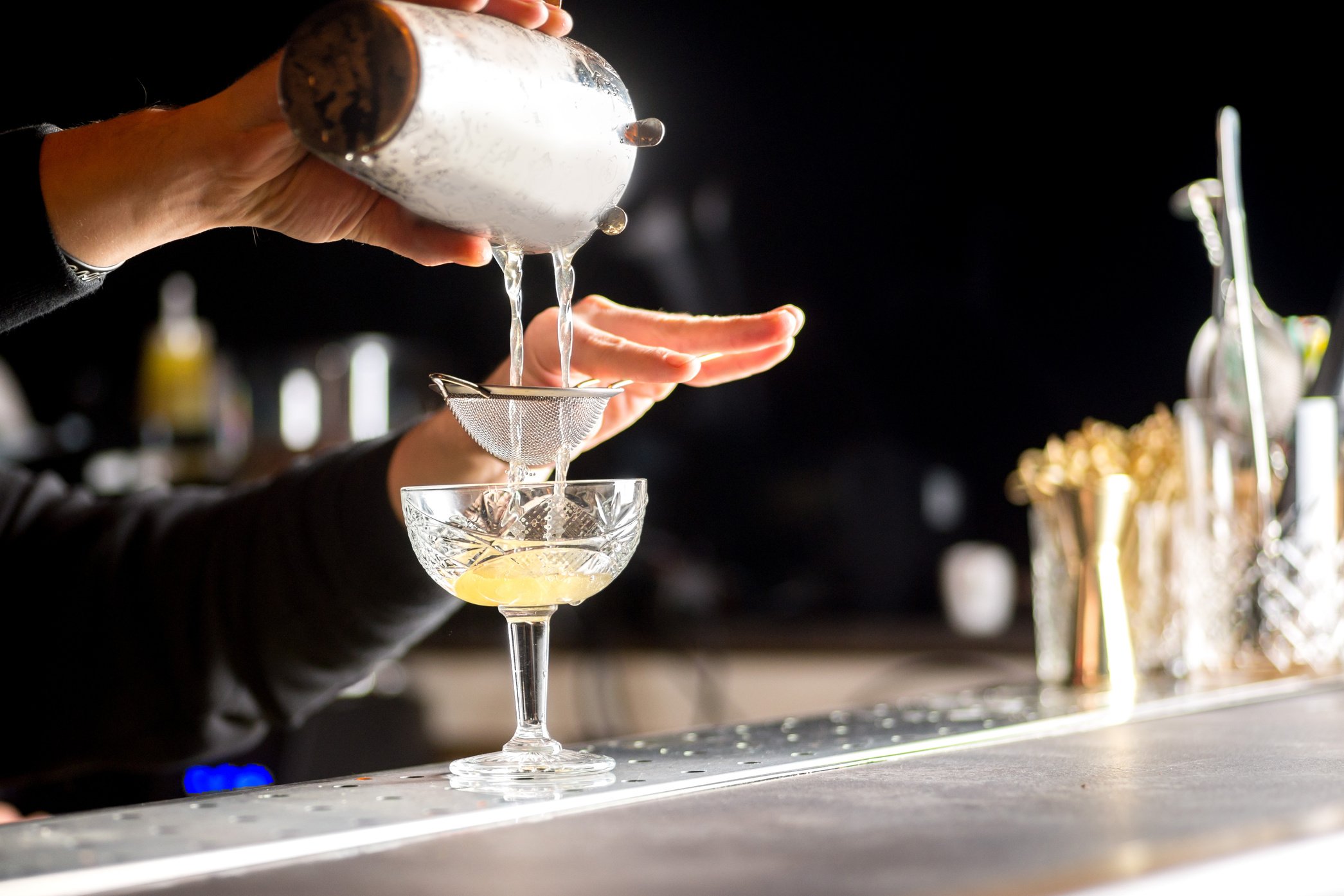 a bartender pours a cocktail into a glass